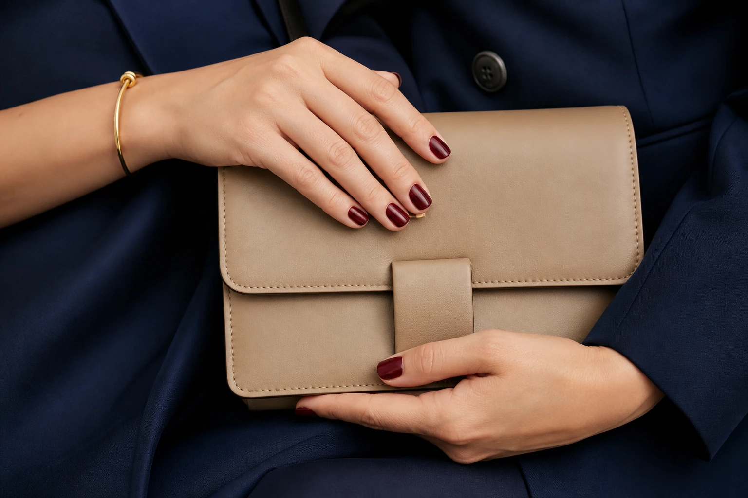 Unhas vinho combinadas com bolsa bege, acessório dourado e roupa azul-marinho